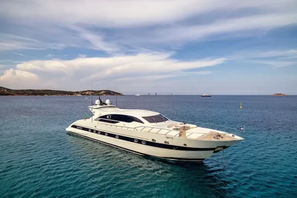 Side view of the Velvet 100 yacht anchored in the crystal-clear turquoise waters of Sardinia under a blue sky.