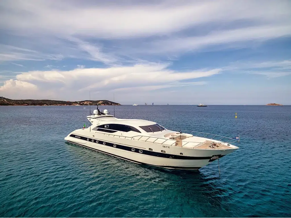 Side view of the Velvet 100 yacht anchored in the crystal-clear turquoise waters of Sardinia under a blue sky.