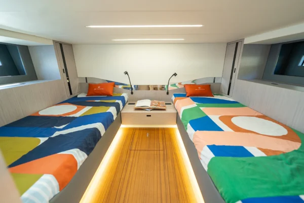 Interior of the BB Yachts Panarea 44 guest cabin showing twin beds with colorful geometric patterns and wood flooring, available for charter in Costa Smeralda, Sardinia.