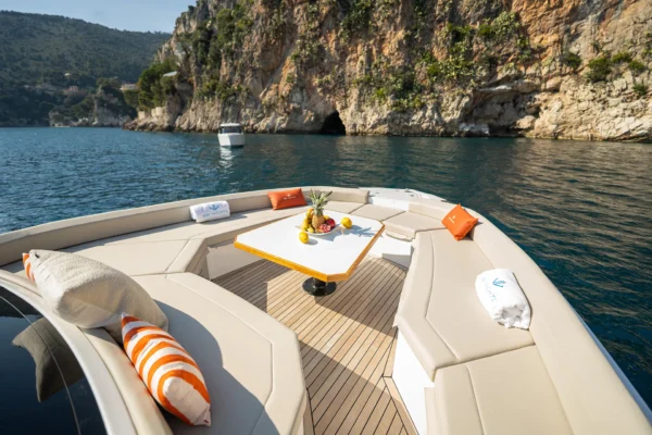 Bow seating arrangement of the BB Yachts Panarea 44 with a central table and beige cushions against the rocky coast of Sardinia.