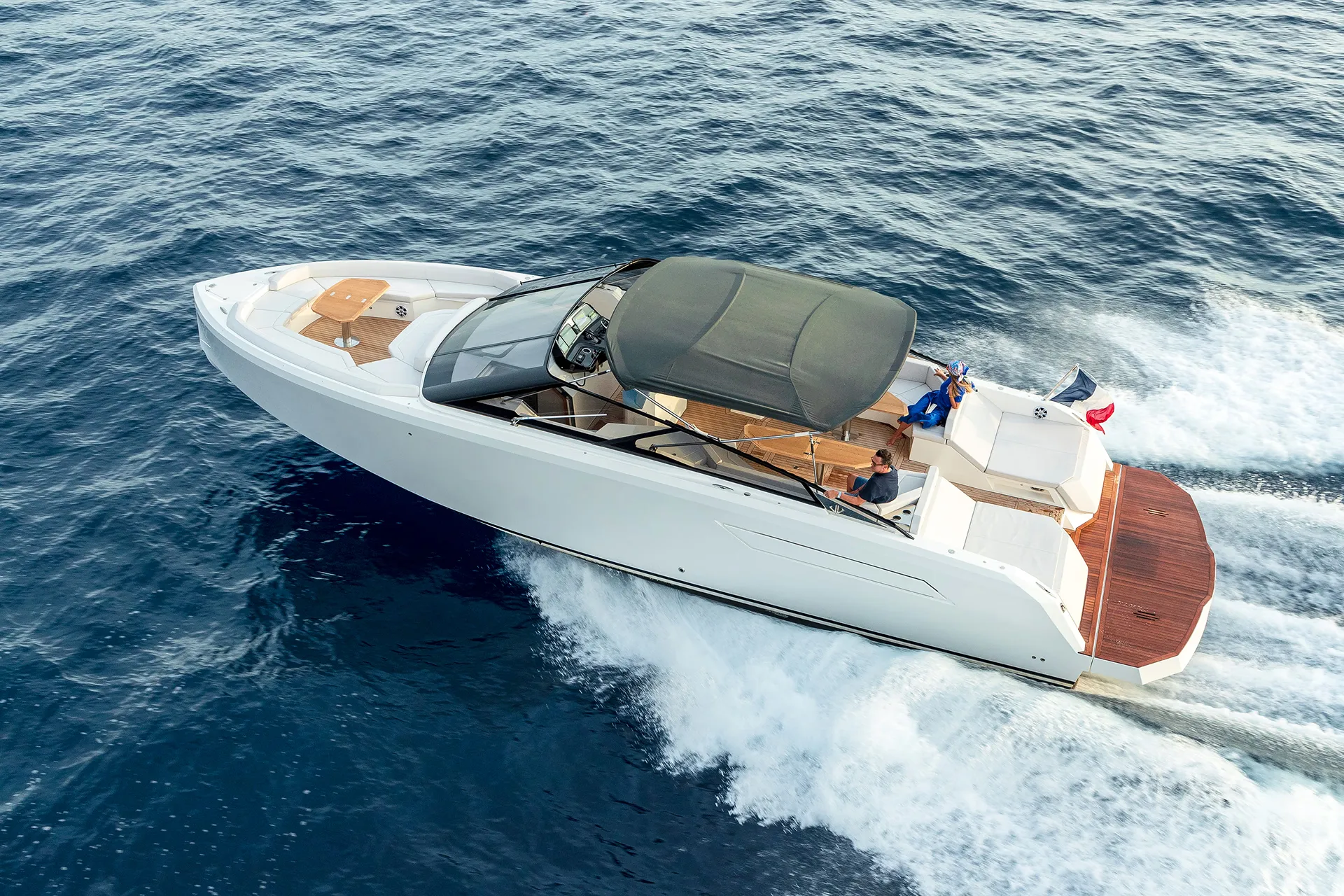 A white BB Yachts Panarea 44 motor yacht cruising at high speed on the Mediterranean sea near Porto Cervo. The image shows the yacht's sleek profile, the large wooden stern platform, the black bimini top, and guests enjoying the navigation in the Costa Smeralda, Sardinia.