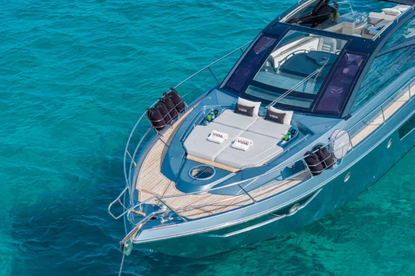 A close-up view of the Cranchi 60 ST bow featuring two large white sunpads on the teak foredeck, positioned against the vibrant blue sea of the Costa Smeralda near Porto Cervo, Sardinia.
