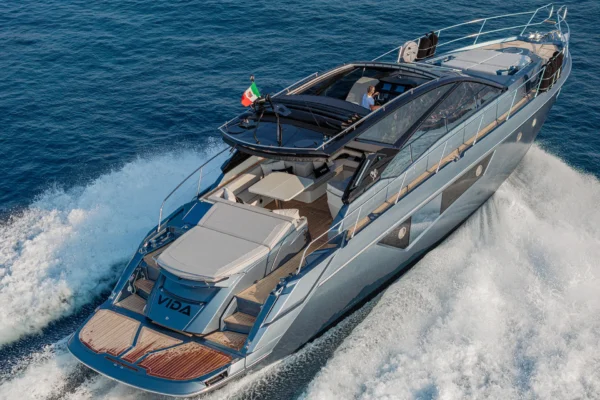 A high-angle side view of a grey Cranchi 60 ST yacht cruising through deep blue water and creating white wake foam while navigating the sea off the coast of Porto Cervo, Costa Smeralda, Sardinia.