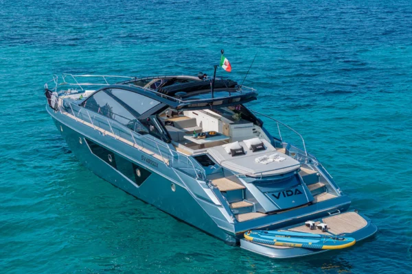 A three-quarter view from the rear of a Cranchi 60 ST on the water, showcasing the stern platform and the modern hull lines as it sits in the Mediterranean waters of Porto Cervo, Costa Smeralda, Sardinia.