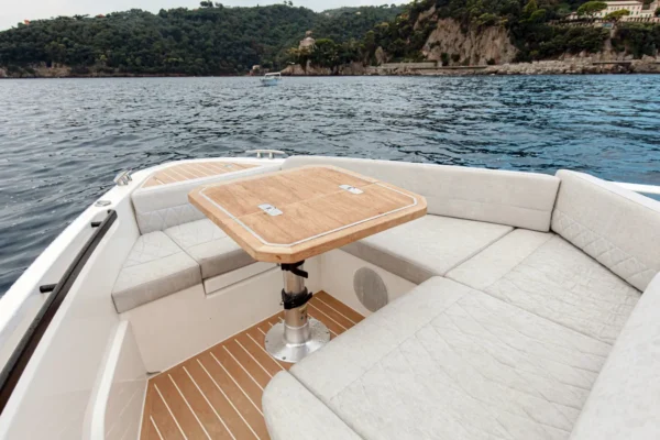 View from the aft deck of the Saxdor 400 GTO looking towards the sea, featuring the L-shaped sofa and teak dining area with the Sardinian coastline in the background.