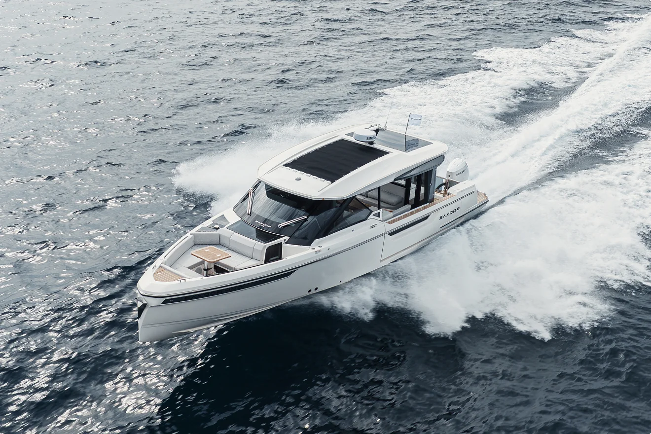 High-performance Saxdor 400 GTO powerboat speeding across deep blue Mediterranean water, creating a large dynamic wake. The image is an aerial view capturing the bow seating area and modern hardtop, perfect for a day charter in Porto Cervo, Costa Smeralda, Sardinia.