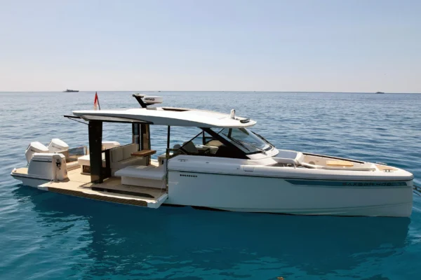 Side profile of a white Saxdor 400 GTO yacht at anchor in a quiet bay near Porto Cervo, showcasing its sleek design and open wheelhouse layout.