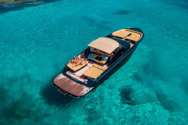 Looking down from an aerial perspective at the aft deck of a dark blue Continental 50 yacht, showing three guests sunbathing on the parallel beige stern mattresses next to the large wooden swim platform.