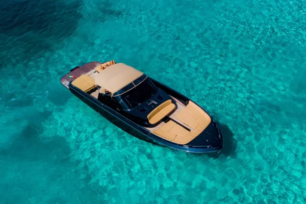 An aerial shot of a dark-hulled Continental 50 open yacht stationary on clear turquoise water, displaying beige cushions on the large bow and aft sunbeds, and a matching beige bimini top over the central console.