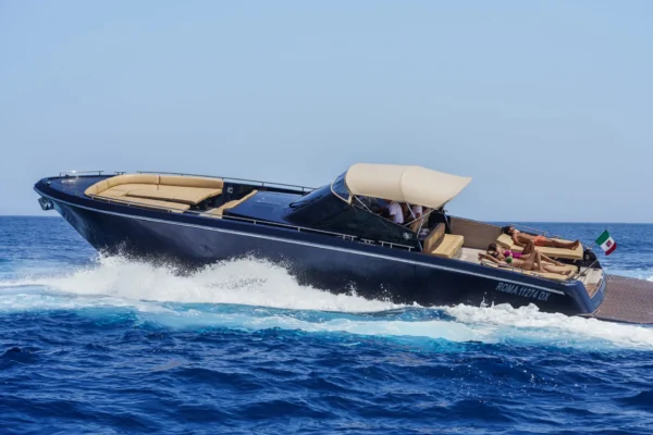 Side view of the dark-hulled Continental 50 motor yacht planing on blue water, showing its sharp bow, beige upholstery, open cockpit with a canvas top, and passengers relaxing on deck.