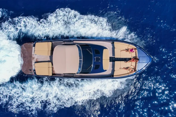 Veduta aerea zenitale di uno yacht Continental 50 in navigazione veloce che lascia una scia di schiuma bianca nel mare blu profondo, con tre ospiti distesi sul prendisole di prua.