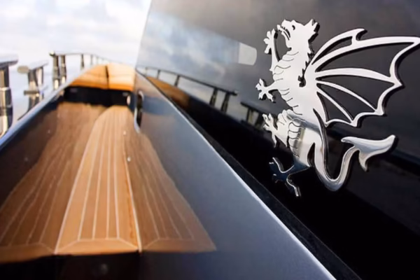 Primo piano del logo cromato a forma di dragone posizionato sulla tuga scura di uno yacht Continental 50, con il teak del passa avnti e il cielo sullo sfondo.