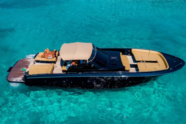 Lo yacht a motore Continental 50 galleggia su un mare turchese e trasparente con il fondale visibile, mentre due ospiti si rilassano sul grande prendisole di poppa sotto il tendalino parasole.