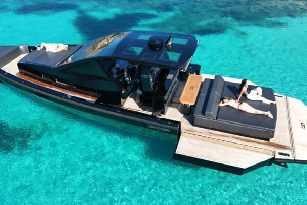 Elevated view of the luxury Seainfinity T5 walkaround yacht at anchor in Porto Cervo, highlighting the expanded 6.42-meter beam with open hydraulic terraces and guests sunbathing on deck.