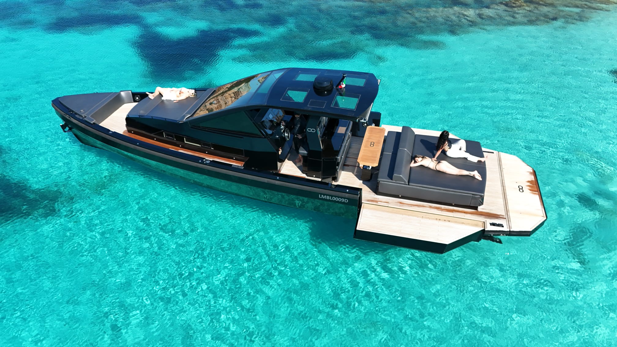 seainfinity-t5-private-beach-club-deck-layout A high-angle drone photograph focusing on the deck layout of the Seainfinity T5 yacht, displaying the seamless connection between the shaded dining area, the large aft sunbed, and the extended side terraces in Costa Smeralda.