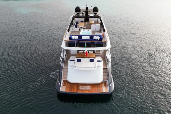 Aerial stern view of the Amer F100 superyacht highlighting the multi-level deck layout, expansive swim platform, aft cockpit dining area, and flybridge featuring a jacuzzi and U-shaped navy blue seating.