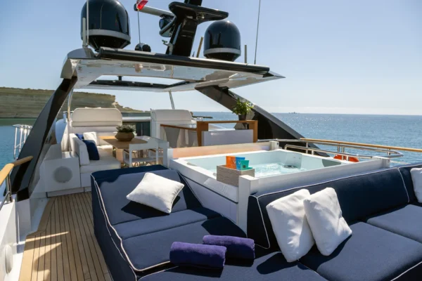 Luxury flybridge deck of the Amer F100 superyacht featuring a jacuzzi, plush navy blue sunpads, and shaded dining lounge area.