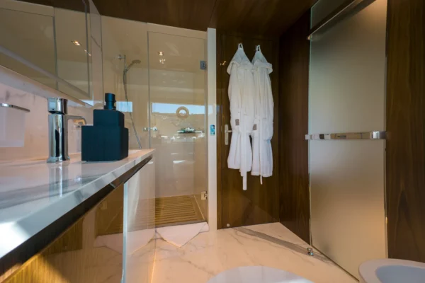 Modern guest bathroom interior on the Amer F100 superyacht, showcasing a sleek white marble vanity with contemporary black accessories, a glass shower enclosure, and high-end dark wood finishes.