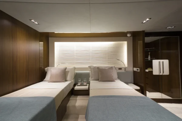 Luxurious twin guest cabin on the Amer F100 superyacht featuring two single beds, elegant wooden wall panels, soft neutral bedding, reading lights, and an en-suite wardrobe space.