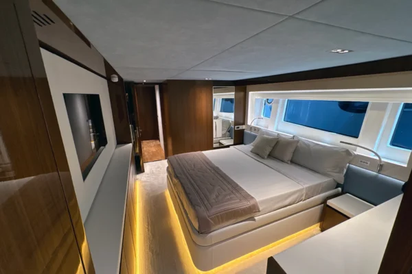 Spacious VIP guest stateroom on the Amer F100 superyacht featuring a central double bed with warm LED base lighting, integrated media screen, high-gloss cabinetry, and large side windows.