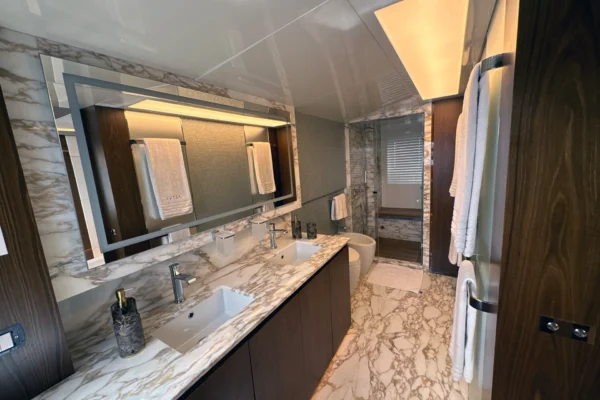 Elegant master en-suite bathroom on the Amer F100 superyacht featuring heavily veined marble flooring and walls, a large dual-sink vanity, modern fixtures, and a spacious glass-enclosed shower.