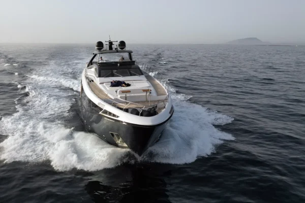 Direct head-on aerial view of the Amer F100 superyacht underway, cutting powerfully through the water to create a dramatic white bow wake, with foredeck lounging areas clearly visible.