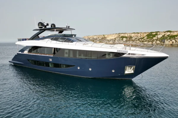 Starboard profile view of the Amer F100 superyacht anchored in clear waters, showcasing its dark blue hull, tinted panoramic windows, sleek white superstructure, and modern exterior lines.