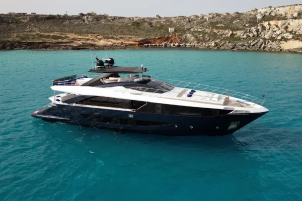 High-angle aerial view of the Amer F100 superyacht in clear turquoise water showcasing its dark blue hull and white superstructure.