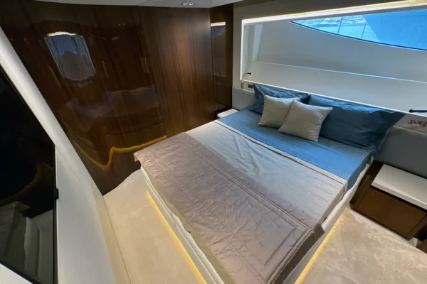High-angle shot of a VIP double stateroom on the Amer F100 superyacht showcasing a plush bed with ambient LED under-lighting, sleek TV console, and high-gloss dark wood paneling.