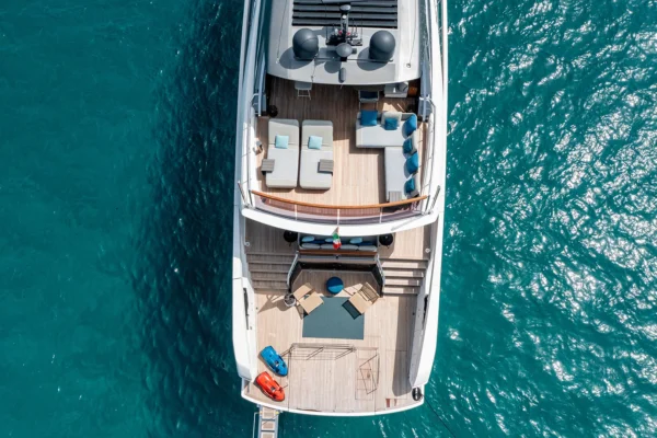 Aerial top-down perspective of the Sanlorenzo SX88 highlighting the furnished flybridge deck, aft cockpit seating, and teak swim platform equipped with red and blue seabobs.