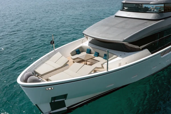 Close up view of the Sanlorenzo SX88 foredeck featuring a spacious teak lounge area with large adjustable sunpads, U-shaped seating, a central table, and teal decorative pillows.
