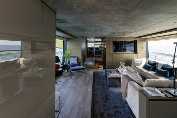 Spacious open-plan living area aboard the Sanlorenzo SX88, showcasing high-gloss wall reflections, comfortable lounge seating, a central staircase, and a clear sightline into the forward dining space.