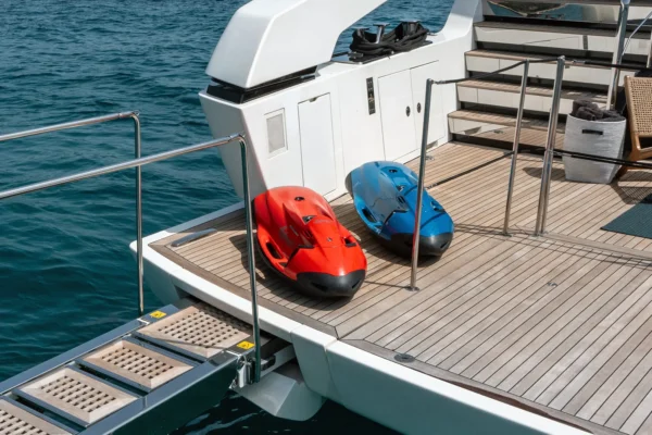 Teak swim platform of the Sanlorenzo SX88 featuring a deployed stainless steel swim ladder and two Seabob water scooters, one red and one blue, resting on the deck.