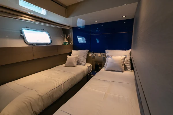 Guest accommodation on the Sanlorenzo SX88 showing a twin cabin configured with bunk beds, featuring crisp white bedding, a glossy blue accent wall, and a porthole window.