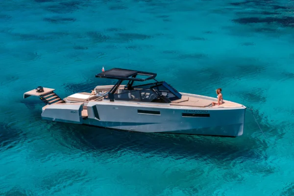 Side profile of the EVO 43 WA yacht anchored in bright blue waters. The image highlights the sleek grey hull, black hardtop, and the raised hydraulic aft platform, with a guest sitting comfortably on the forward sunpad.