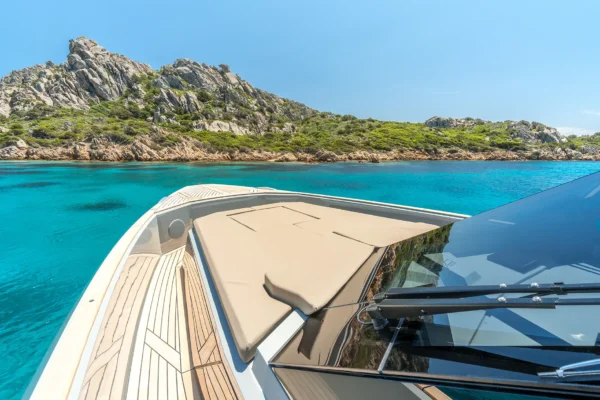 View from the helm looking forward over the bow of the EVO 43 WA motor yacht. The image highlights the spacious beige sunpad, the black tinted windshield, and the walk around teak deck, with the boat anchored in clear turquoise waters.