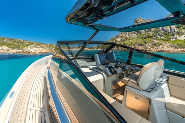 View of the modern helm station on the EVO 43 WA motor yacht. The cockpit features dual navigation displays, a steering wheel, pilot seating, an angular black-framed windshield, and a clear view of the port side walk around teak deck under the open hardtop.