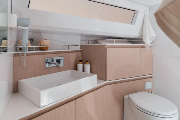 Interior view of the modern bathroom on the EVO 43 WA motor yacht. The space features light wood cabinetry, a white rectangular vessel sink with a chrome faucet, a white toilet, a wall-mounted hairdryer, and a horizontal window providing natural light.