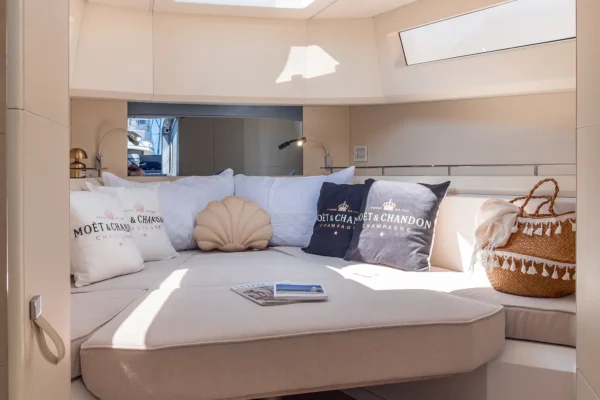 Bright and modern interior view of the lower deck cabin on the EVO 43 WA yacht. The space features a large, comfortable V-berth bed with light beige upholstery, decorative pillows, side windows, and an overhead skylight letting in natural sunlight.